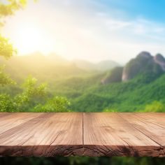 an empty wooden table in front of a mountain range with sunlight streaming through the trees