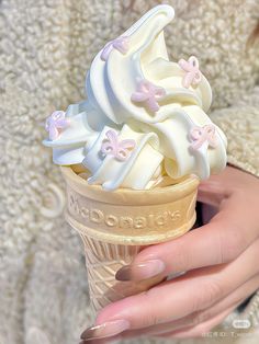 a woman holding an ice cream cone with white frosting and pink flowers on it