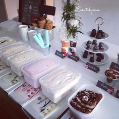 an assortment of desserts on display at a buffet table with signs and flowers in the background