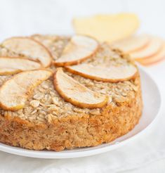 an apple and oatmeal cake on a plate with sliced apples in the background