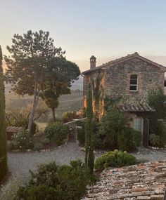 an old stone house surrounded by greenery in the countryside at sunset, with trees and bushes surrounding it