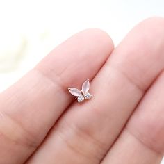 a person holding a tiny butterfly shaped stud in their left hand, with the tip of it's nose visible