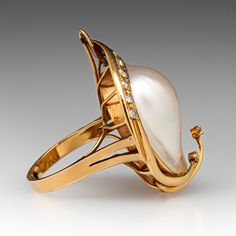 This gorgeous 18k yellow gold ring is centered with one (1) blister pearl set into a bezel. Two ribbons of yellow gold that extend over the blister pearl are accented with two (2) prong set round brilliant cut diamonds. The blister pearl is bordered with ten (10) bead set round single cut diamond accents. The ring measures 33.9mm at the top, rises 3.9mm above the finger, and tapers to 2.8mm wide by 1.0mm thick at the base of the shank.  The ring is currently a size 6.75. Fine Jewelry Yellow Gold Pearl Ring With High Luster, Yellow Gold Pearl Ring With High Luster, Formal Yellow Gold Pearl Ring With Rose Cut Diamonds, Formal 14k Gold Pearl Ring With High Luster, Formal Yellow Gold Pearl Ring With High Luster, Formal High Luster Yellow Gold Pearl Ring, Luxury Yellow Gold Pearl Ring With Cabochon, Anniversary Yellow Gold Pearl Ring With Cabochon, Luxury Cabochon Pearl Ring For Wedding