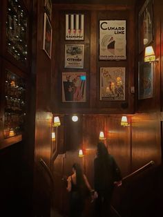 two people are walking up the stairs in a dark room with posters on the wall