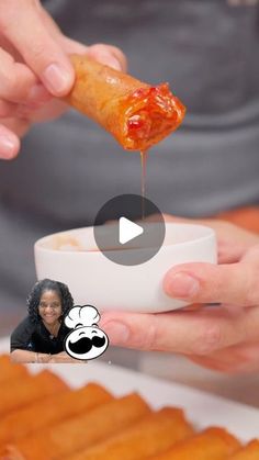 a person is dipping something into a small bowl with sauce on it and another hand holding the food in front of them