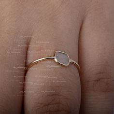 a woman's hand wearing a gold ring with a white stone on it,