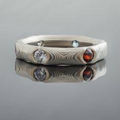 This custom 3.5mm Mokume Gane band is shown in the Guri Bori pattern and the Smoke metal combination with six 2.5mm flush-set diamonds, blue topaz, and amethyst and an etched finish. The Smoke palette features 14k white gold, palladium, and sterling silver.Pattern: Guri BoriPalette: SmokeFinish: EtchedProfile: Low DomeWidth Shown: 3.5mm Stones: 6 (2.5mm) flush-set diamonds, blue topaz, and amethyst Added: extra thickness **Prices do NOT include stones or setting fees.** SPECIAL PRICING FOR SETS. Modern Multi-stone Wedding Jewelry, Ceremonial Silver Diamond Ring, Fusion Single Cut Diamonds Jewelry For Anniversary, Fusion Style Jewelry With Single Cut Diamonds For Anniversary, Fusion Style Single Cut Diamonds Jewelry For Anniversary, Fusion Style Polished Wedding Jewelry, Modern Multi-stone Round Cut Jewelry, Flush Set Diamond, Mokume Gane