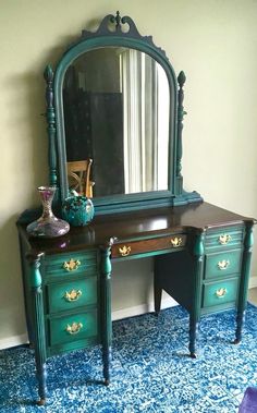 an antique desk with mirror and vase on it in front of a blue carpeted wall