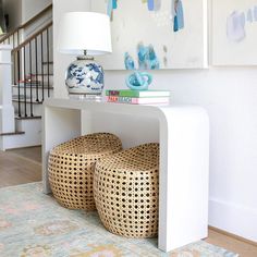 two wicker stools under a table with books on it and a lamp next to them