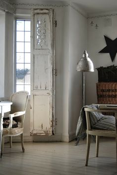 an old door in the corner of a room next to a chair and table with a lamp on it