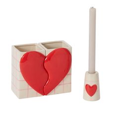 a red heart shaped candle holder next to a white cup with a stick in it