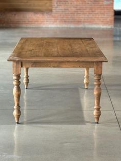 a wooden table sitting on top of a cement floor next to a brick wall in an empty room