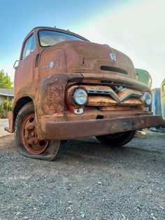 an old rusted truck is parked on the gravel in front of some other trucks