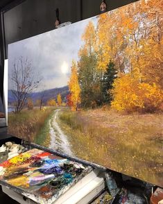 an artist's easel with paint and brushes on it in front of a painting