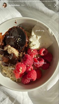 a bowl filled with ice cream, raspberries and chocolate covered dessert on top of a white cloth