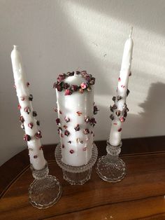 three white candles with pink and purple flowers on them sitting on a table next to each other