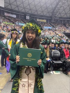 a woman in a green graduation gown holding up a sign with her mouth wide open