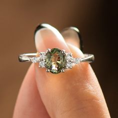 a close up of a person's hand holding a ring with an oval shaped green diamond