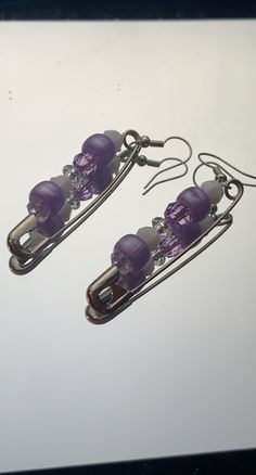 two pairs of earrings with purple beads hanging from hooks on a white surface, next to each other