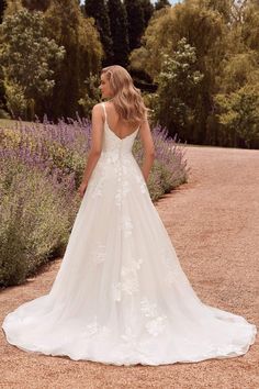 a woman in a wedding dress standing on a dirt road with lavender bushes behind her