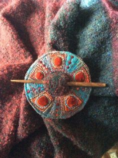 an orange and blue brooch with two wooden sticks in front of it on a blanket