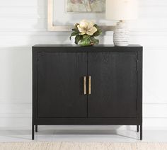 a black cabinet with two doors and a white flower on top in front of a painting