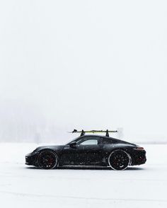 a black sports car with skis on top parked in the middle of a snow covered field