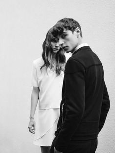 a young man and woman standing next to each other in front of a white wall