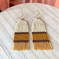 the beaded earrings are hanging from hooks on a wooden table with white and brown beads