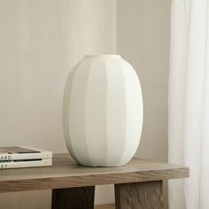 a white vase sitting on top of a wooden table next to a bookshelf