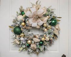 a christmas wreath on the front door with green and gold ornaments hanging from it's sides