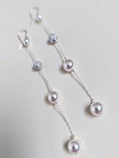 three pairs of pearl and diamond earrings on a white surface, with the pearls dangling from them