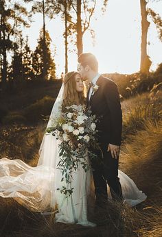 a bride and groom standing in the woods at sunset