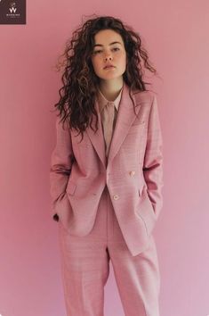 a woman in a pink suit standing against a pink wall with her hands on her hips