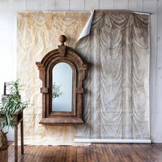 an old mirror sitting on top of a wooden floor next to a wall with curtains