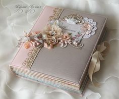 a pink book with flowers and lace on it sitting on a white bed sheet next to a ribbon