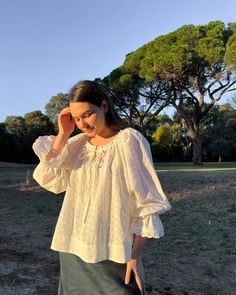 a woman in a white blouse is walking through the grass and talking on her cell phone