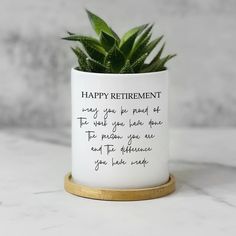 a plant in a white ceramic pot that says happy retirement on the bottom and gold rimmed base