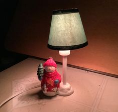 a lamp that is on top of a table with a snowman figurine next to it