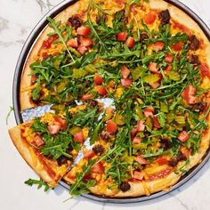 a pizza sitting on top of a metal pan covered in greens and toppings next to a knife