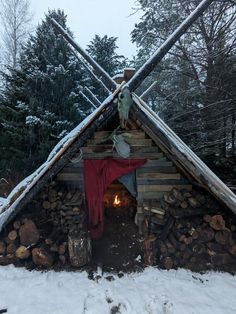 a small cabin made out of wood and logs in the snow with a red cloth draped over it