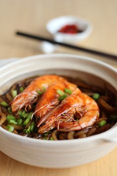 a bowl filled with shrimp and vegetables next to chopsticks on a wooden table