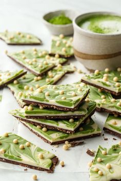 there are many pieces of green and white food on the table with some cups in the background