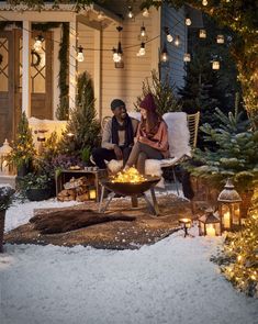 two people sitting on chairs in front of a house with christmas lights hanging from the roof