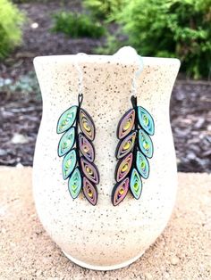 a pair of colorful earrings sitting on top of a white vase