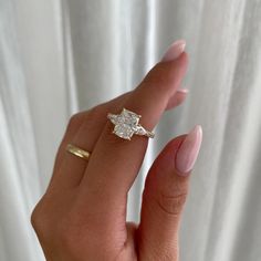 a woman's hand holding a diamond ring in front of a white curtain,