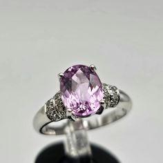 Indulge in the timeless allure of this vintage estate ring, crafted in luxurious 18k white gold. The focal point is a resplendent oval-cut kunzite, boasting a substantial 2.08 carats. Kunzite, known for its positive properties, brings a gentle, soothing energy and is often associated with matters of the heart. The captivating pink hue of the genuine kunzite is cradled in an elegant 4-prong setting, exuding a soft and romantic charm. Adorning the shoulders of the ring are genuine natural diamonds Classic Sapphire Ring In 14k White Gold, Exquisite Oval Platinum Gemstones, Luxury Solitaire Amethyst Ring, Elegant Brilliant Cut Gemstone For Anniversary, Classic Round Gemstones With Center Stone, Elegant Oval Brilliant Cut Gemstones, Elegant Topaz Ring With Center Stone, Classic Round Cut Ruby For Promise Ring, Classic Round Cut Promise Ring Gemstones