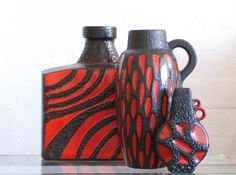 two black and red vases sitting next to each other on a glass table top