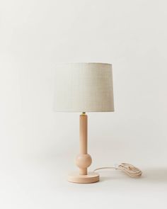 a small wooden table lamp with a white shade on the base and a cord plugged into it