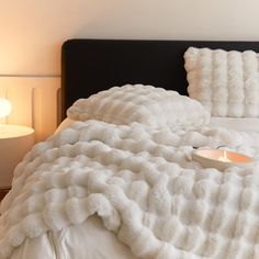 a bed with a white comforter and a lit candle on the end of it